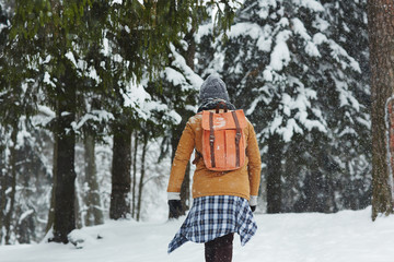 Young man with backpack walking down in snowdrift on winter day during trip in the forest