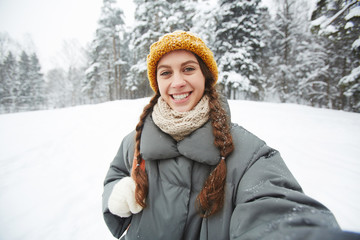 Obraz premium Young smiling woman with backpack making selfie on winter day in natural environment