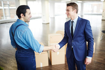 Fototapeta na wymiar Young businessman in suit and delivery man in uniform handshaking after relocation work
