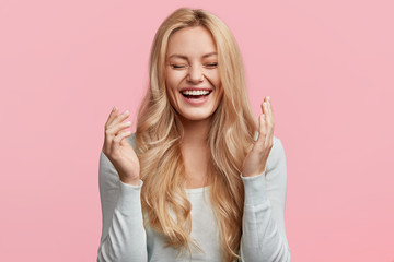 Isolated shot of joyful blonde young cute woman laughs joyfully as hears funny anecdote from...
