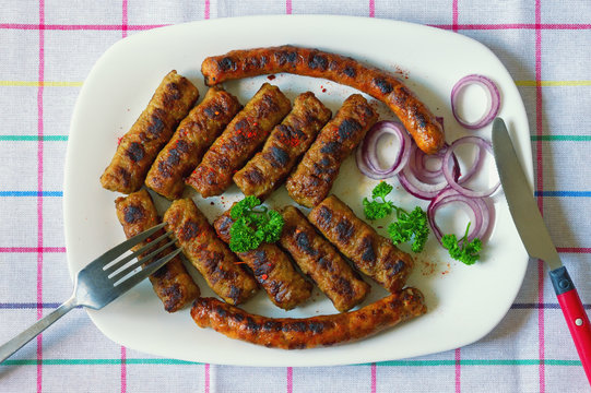 Balkan cuisine. Cevapi and kobasica  - grilled dish of minced meat - on white plate. Flat lay