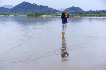 Asian female tourist using mobile phone taking beautiful picture of Nong Khai Grand Canyon or Phan Khot Saen Khrai in Mekong river , Nong Khai , Thailand