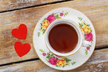 Black tea in vintage porcelain cup and two red hearts on wooden surface
