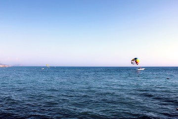 Fototapeta premium Blue Mediterranean sea. People fly by parachute in the blue sky over the sea in clear weather, a holiday at sea, parachute flying over the sea, towing by a boat