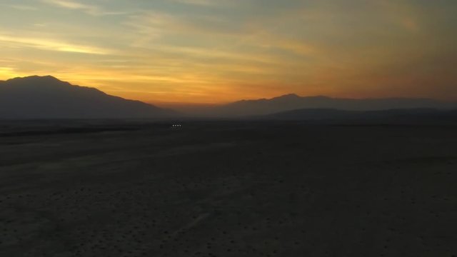 Aerial panning shot while zooming out of sunset behind mountains
