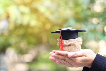 Woman hand holding coins money in a bag with graduates hat on natural green background, Saving money for education concept