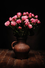 Dark Dutch painters style classic still life with pink roses in rustic brown clay vase on wooden table. Example for art school.