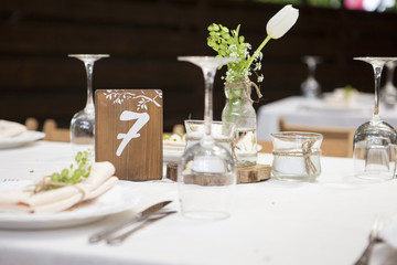 Simple but luxury rich table setting for a wedding celebration in nice cozy restaurant. Wineglasses, plates and bouquet of summer seasonal flowers on a table. Sunlight from a window. Copy space