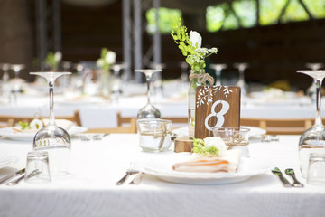 Simple but luxury rich table setting for a wedding celebration in nice cozy restaurant. Wineglasses, plates and bouquet of summer seasonal flowers on a table. Sunlight from a window. Copy space