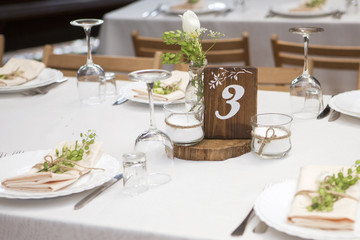 Simple but luxury rich table setting for a wedding celebration in nice cozy restaurant. Wineglasses, plates and bouquet of summer seasonal flowers on a table. Sunlight from a window. Copy space