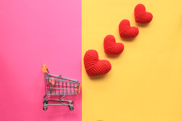 Mini shopping cart and red handmade crochet heart on yellow and pink background for valentines day