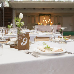 Simple but luxury rich table setting for a wedding celebration in nice cozy restaurant. Wineglasses, plates and bouquet of summer seasonal flowers on a table. Sunlight from a window. Copy space