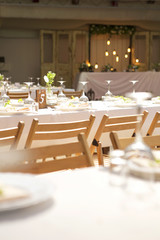 Simple but luxury rich table setting for a wedding celebration in nice cozy restaurant. Wineglasses, plates and bouquet of summer seasonal flowers on a table. Sunlight from a window. Copy space