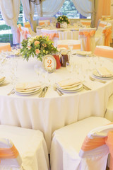 Simple but luxury rich table setting for a wedding celebration in nice cozy restaurant. Wineglasses, plates and bouquet of summer seasonal flowers on a table. Sunlight from a window. Copy space