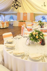 Simple but luxury rich table setting for a wedding celebration in nice cozy restaurant. Wineglasses, plates and bouquet of summer seasonal flowers on a table. Sunlight from a window. Copy space