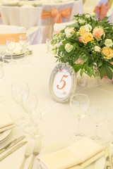 Simple but luxury rich table setting for a wedding celebration in nice cozy restaurant. Wineglasses, plates and bouquet of summer seasonal flowers on a table. Sunlight from a window. Copy space