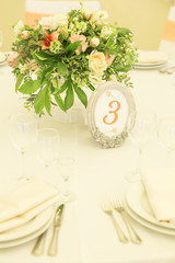 Simple but luxury rich table setting for a wedding celebration in nice cozy restaurant. Wineglasses, plates and bouquet of summer seasonal flowers on a table. Sunlight from a window. Copy space