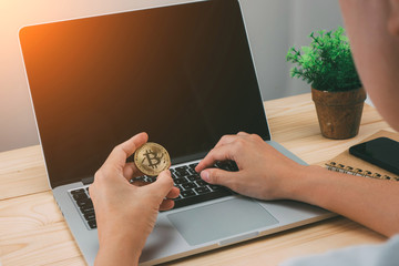 Hand holding golden Bitcoin on computer laptop.