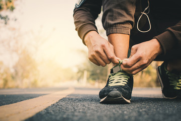 Fototapeta premium Close-up hands of man tying shoelace during running on the road for health, color of vintage tone selective and soft focus