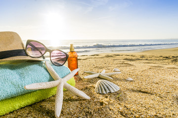 Sunglasses, towels, hat, sun block, shells and starfish on sandy beach