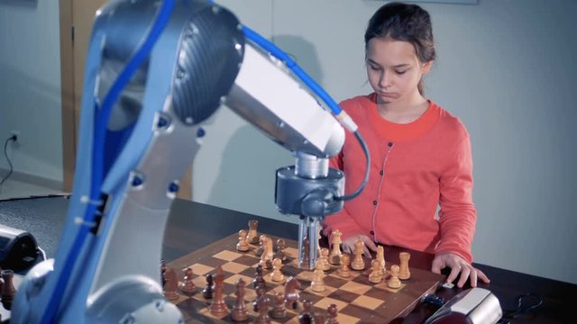 Robotic arm and a little girl are moving chess pieces and playing