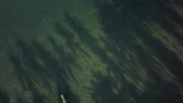 Aerial camera angled down at the green sea with long palm tree shadows, then angles up to show a small fishing boat and more islands in the distance.