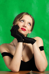 Dreaming girl in evening dress sitting at table. Studio portrait in retro style