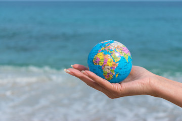 Human hand is holding small globe in front of the sea. Travel and global issues concept.