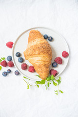 croissant on a plate decorated with mint leaves and fresh berries of raspberries and berries