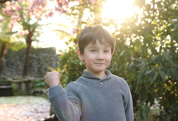 niño en un jardín al atardecer doblando su brazo para demostrar que es fuerte