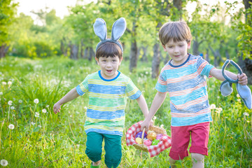 Kids on Easter egg hunt in blooming spring garden. Children searching for colorful eggs in flower...