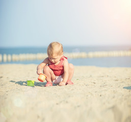 Baby playing on the sandy beach near the sea. Cute little girl in red dress with sand on tropical beach. Ocean coast.