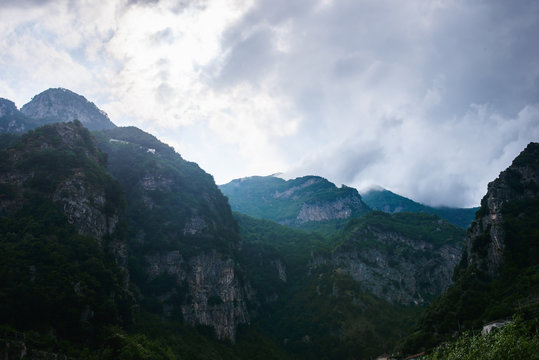 Green mountains in the clouds with rain and fog and blue rock at background. Touristic picture of jungle and rainforest, taken in Amalfi coast, in Italy