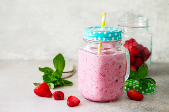 Mason jar mugs with fresh berry smoothies and fresh strawberries and raspberries on a gray stone or slate background. The concept of proper nutrition and health or detoxification. Copy space.