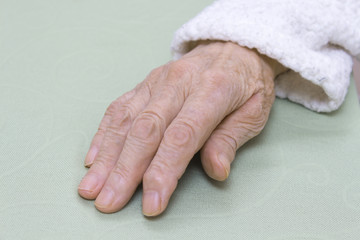 Stara zniszczona skóra dłoni bardzo starej kobiety w białym szlafroku na jasnym tle. Ręka...