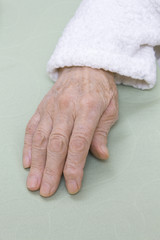 Stara zniszczona skóra dłoni bardzo starej kobiety w białym szlafroku na jasnym tle. - obrazy, fototapety, plakaty