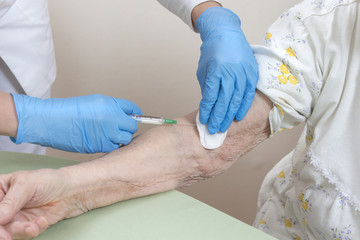Pielęgniarka w rękawiczkach jednorazowych dezynfekuje miejsce na ręce starej kobiety przed...