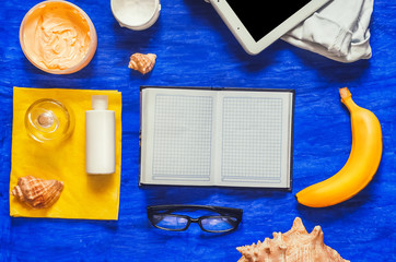 empty notepad. bananaglasses for sight. working space. table. blue background. view from above. perfume, cream, denim shorts