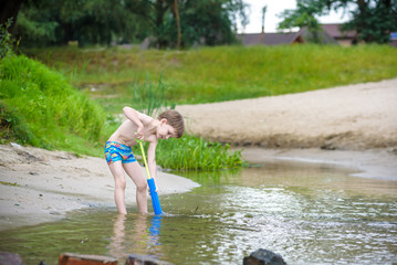 Portrait of caucasian little boy in straw hat playing toys and water pump on the beach.