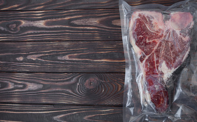 Vacuum sealed fresh beef meat on wooden background. Top view
