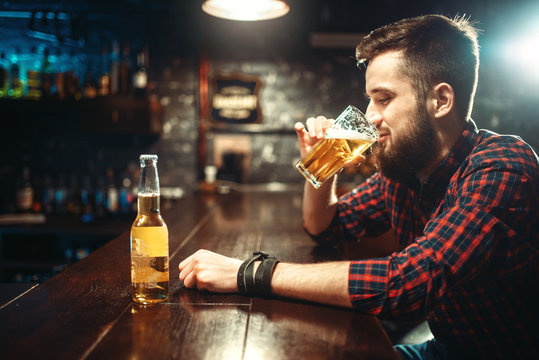 One bearded man drinks beer at the bar counter