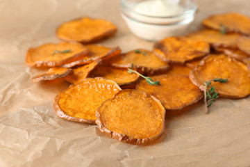 Parchment with tasty sweet potato chips on table, closeup