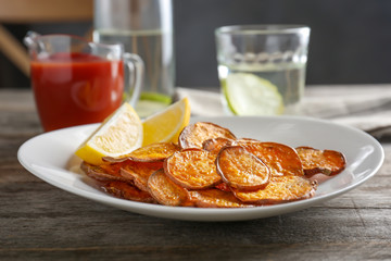 Plate with tasty sweet potato chips on table