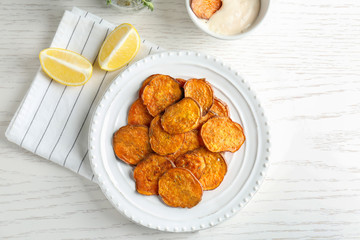 Plate with tasty sweet potato chips on wooden table, top view