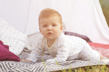 Little newborn infant baby boy kid on a plaid in park. Summer sunset. Copy space