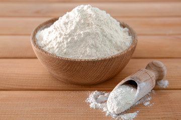 Scoop an bowl of wheat flour on wooden table