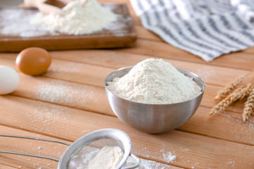 Wheat flour in metallic bowl on wooden table