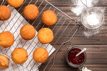 Cooling rack with tasty cupcakes, jar of jam and sugar powder on table. Fresh from oven