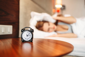 Alarm clock, woman covering her ears with pillow