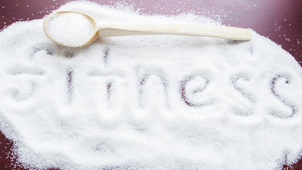 the word FITNESS written on a covered sugar and a wooden spoon on the table.